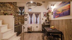 A dining area with a wooden floor, a dining table with chairs, a microwave, and a painting on the wall. - Petrella's Point Studio with AC (Vernazza)