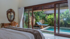 A bedroom with a large bed, a wooden dresser, a mirror, and a sliding glass door leading to a pool area with a chair and a lounge chair. - Dana's Place Private Villa (Ubud)