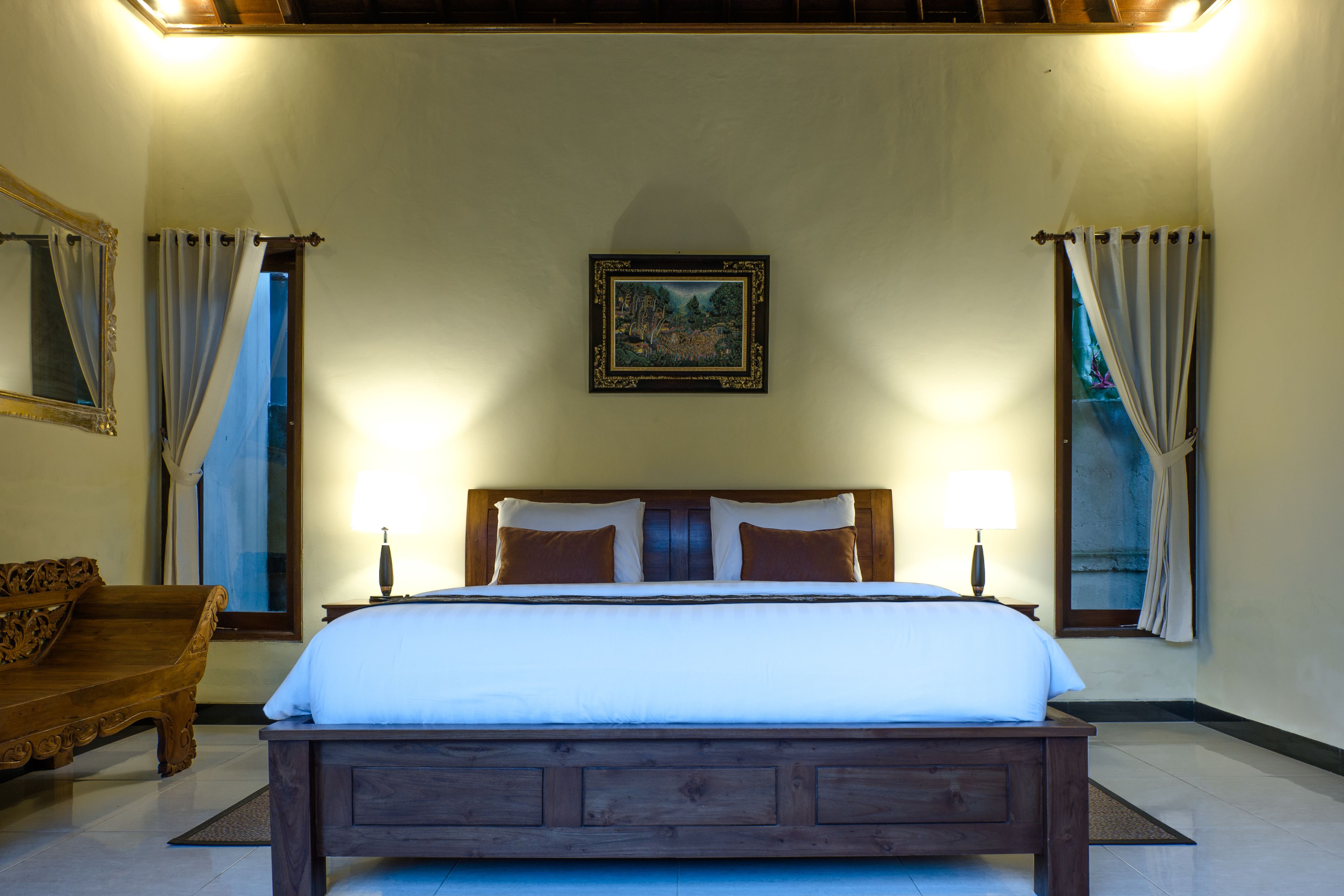 A neatly made bed with a wooden headboard, two bedside lamps, and a framed picture on the wall.