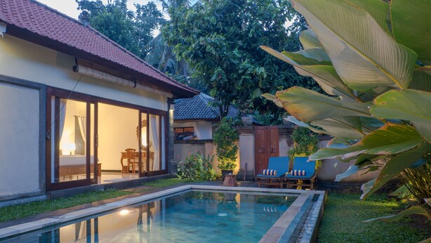 A swimming pool with a tiled deck, a wooden deck chair, and a dining area with a table and chairs. - Dana's Place Private Villa (Ubud)