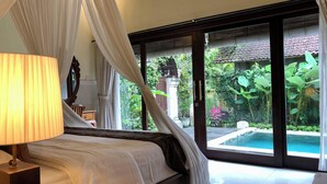 A bedroom with a bed, a bedside lamp, and a view of a swimming pool through large glass doors. - Dana's Place Private Villa (Ubud)