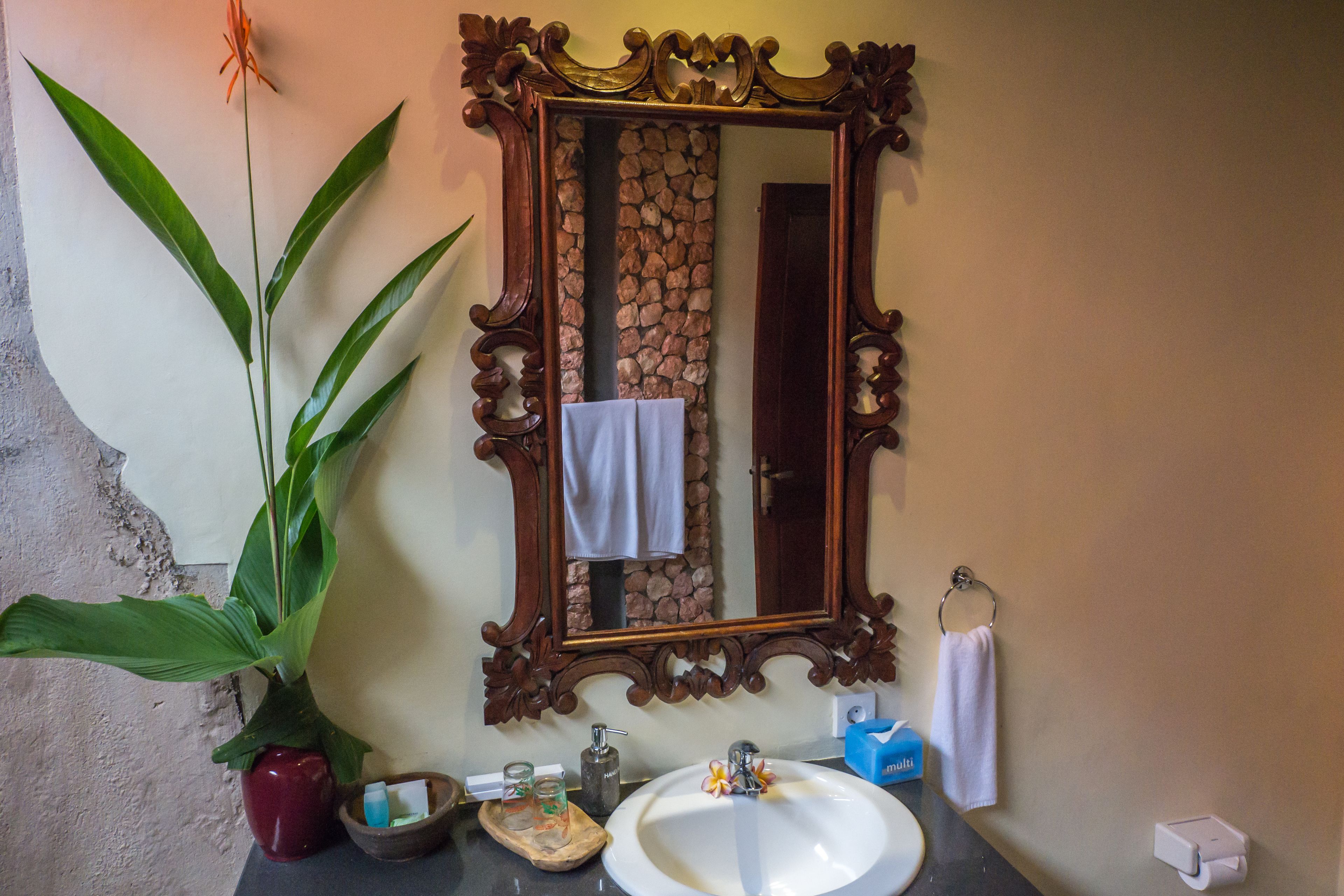 Un baño con un espejo grande, un lavabo, una planta en maceta y un perchero para toallas.