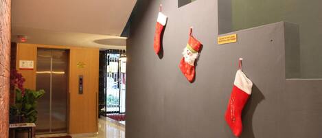 Un pasillo con un ascensor de madera, un bote de basura amarillo y tres calcetines navideños rojos sobre una pared gris.