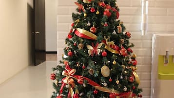 Een kerstboom versierd met decoraties en linten, geplaatst in een gang met een witte bakstenen muur en een deur op de achtergrond.