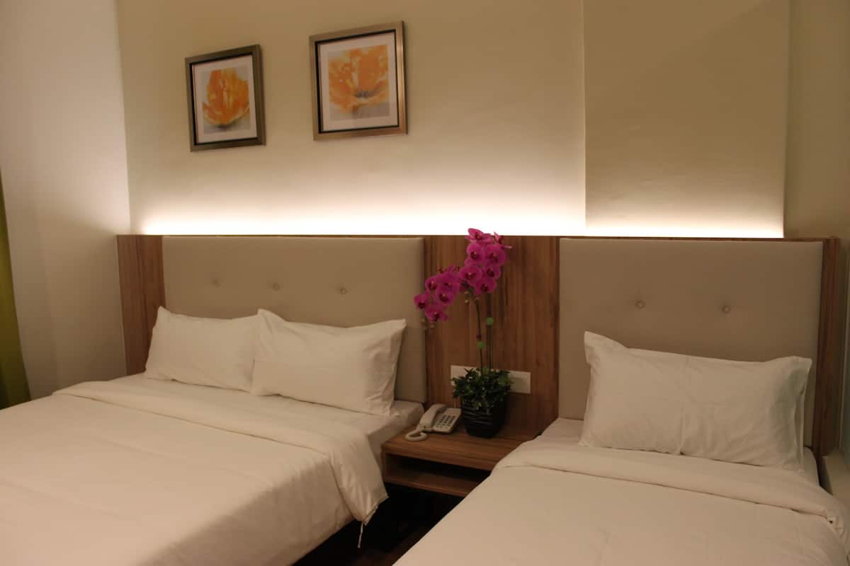 A hotel room with two beds, a nightstand with a phone, and a potted orchid.