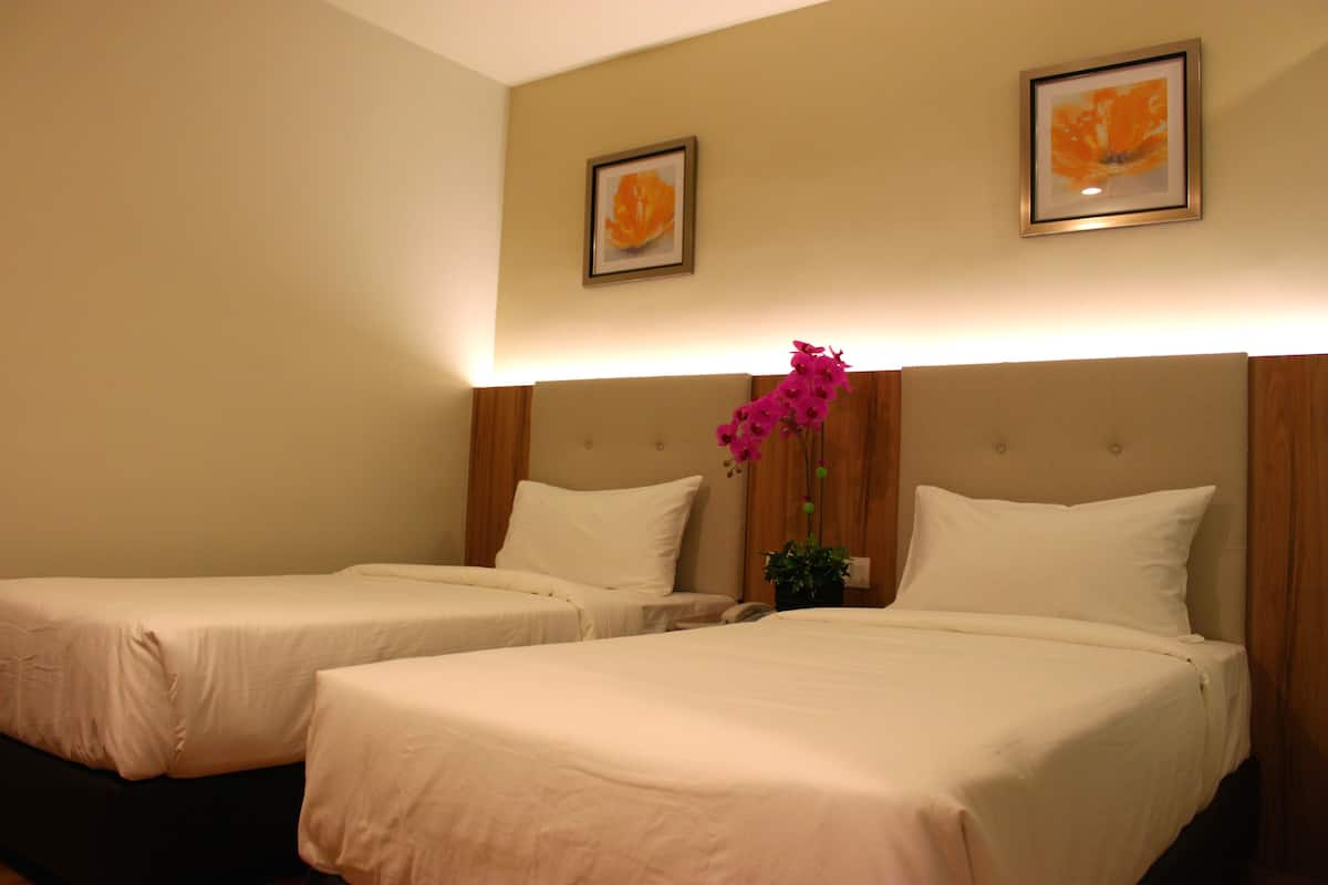 A hotel room with two single beds, a wooden headboard, and a potted plant with pink flowers.
