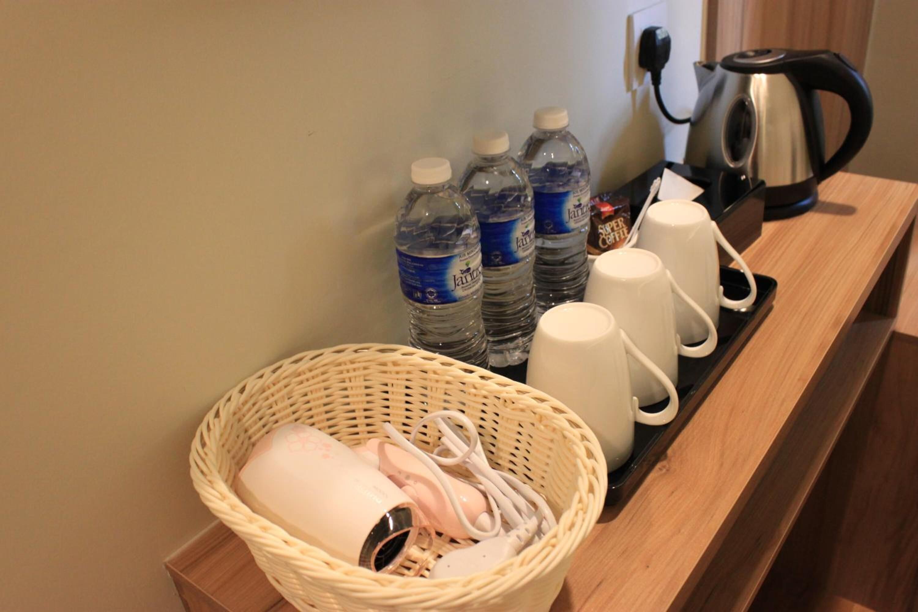 Habitación de hotel con una mesita de madera que sostiene una cesta, botellas de agua, una tetera y una cafetera.