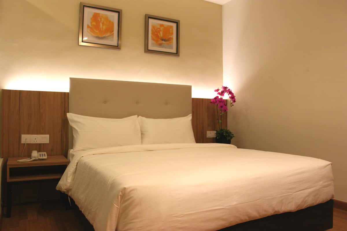 A neatly made bed with white linens, a wooden nightstand with a phone, and a wall-mounted light fixture.