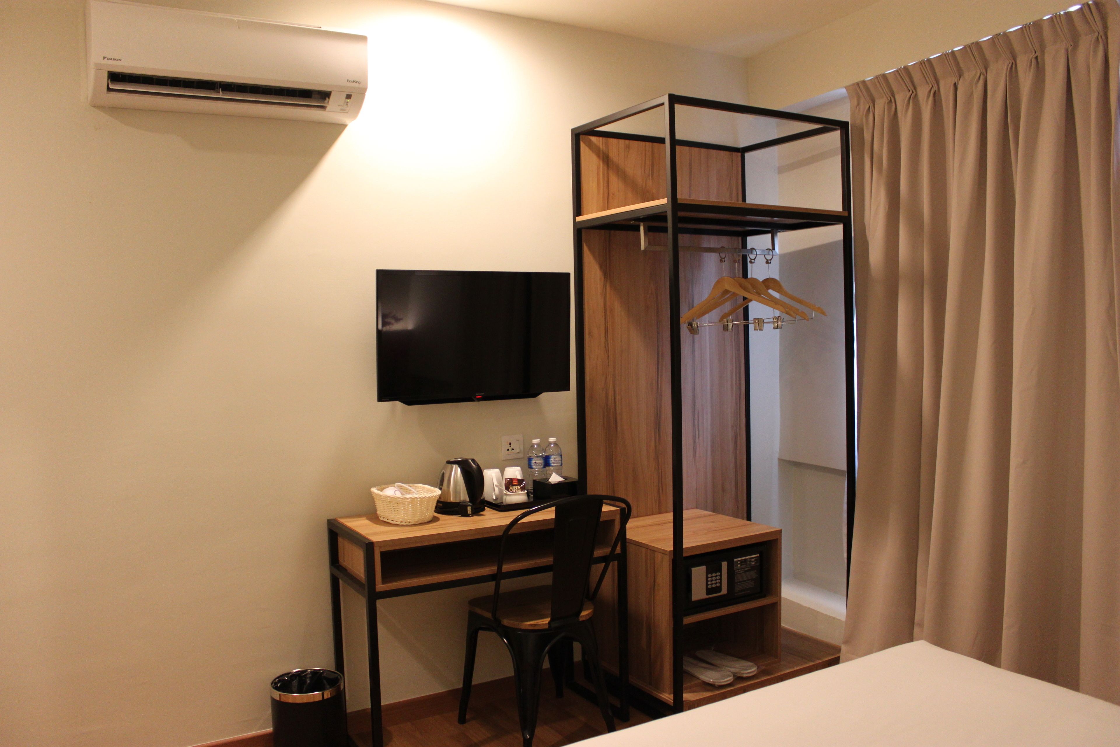 A hotel room with a desk, chair, TV, and a wardrobe with a hanging rack.