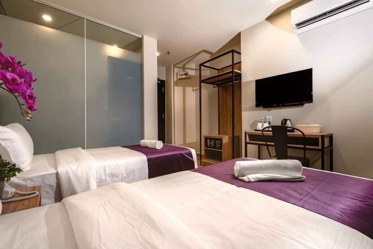 A hotel room with two beds, a desk, a TV, and a shower area.