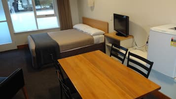 Habitación de hotel compacta con una cama individual, un escritorio pequeño con televisor, refrigerador y ventana con cortinas.
