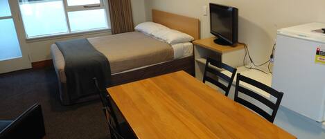 Habitación de hotel compacta con una cama individual, un escritorio pequeño con televisor, refrigerador y ventana con cortinas.