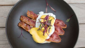 En sort tallerken med en morgenmadsret bestående af æg, bacon og grønt.