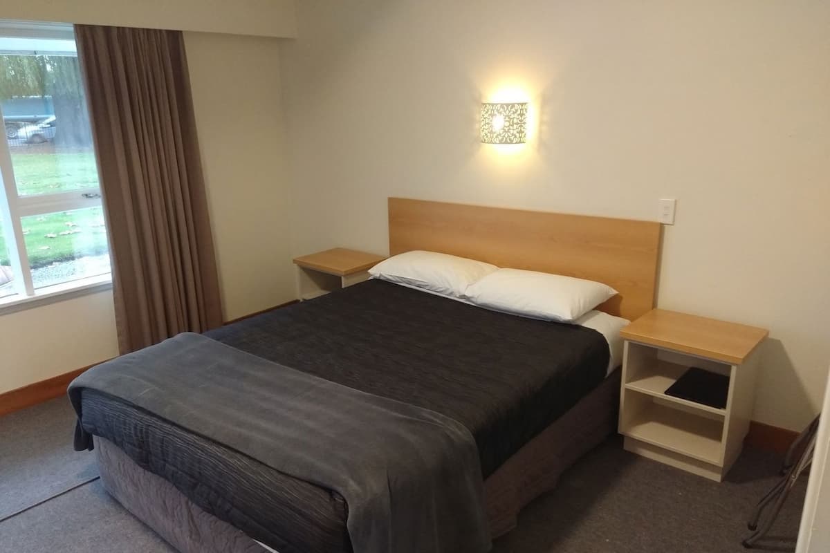 Een hotelkamer met een bed, nachtkastjes, een bedlampje, een raam met gordijnen en uitzicht op de omgeving.