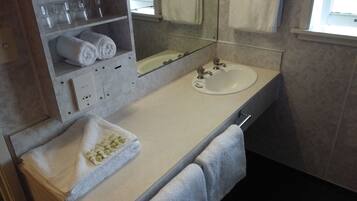A bathroom with a sink, mirror, and towel rack. There are towels and a glass set on the counter.