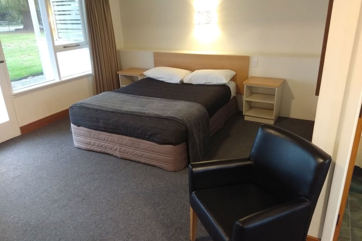 Een hotelkamer met een bed, nachtkastjes, een stoel en een raam met gordijnen.