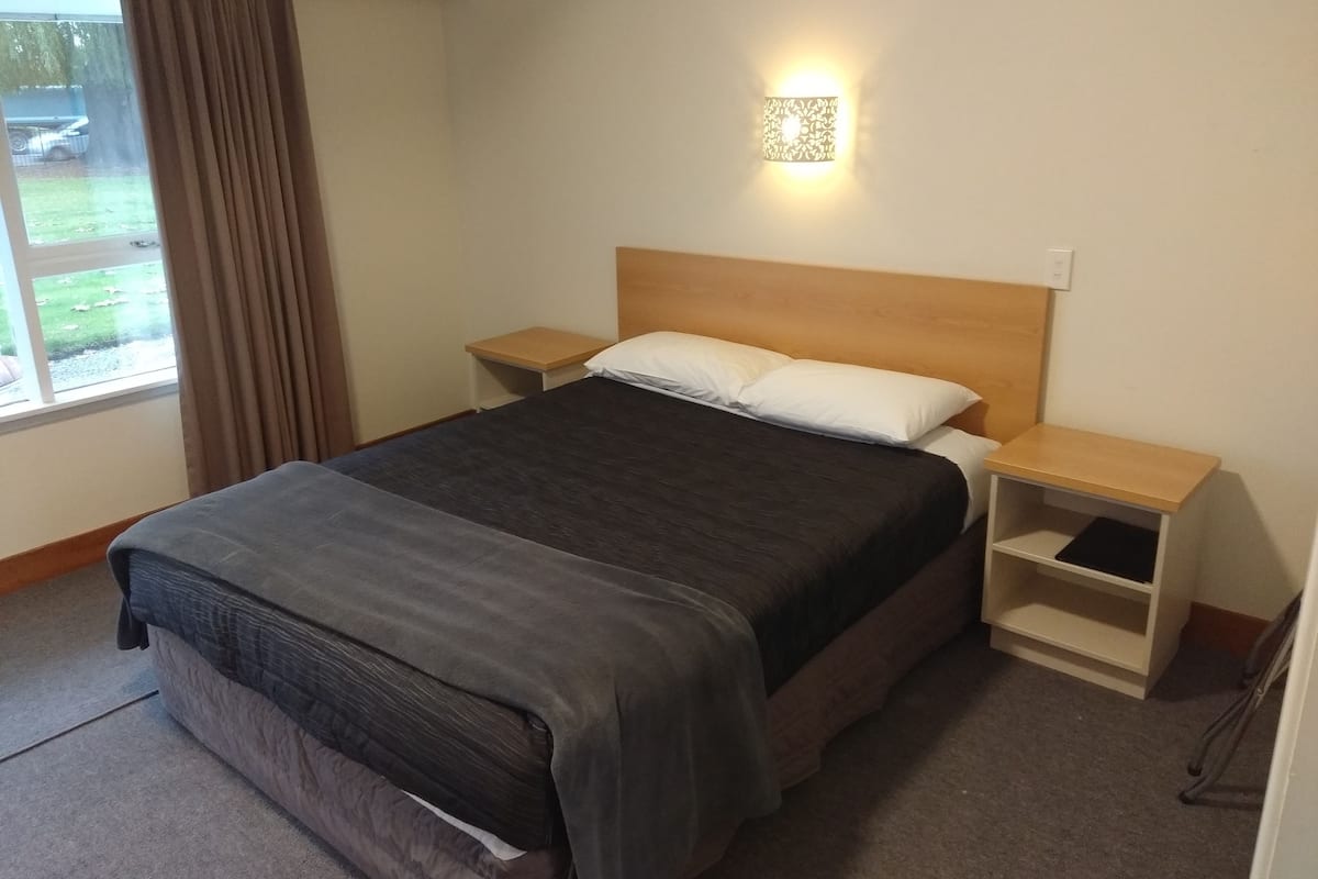Een hotelkamer met een bed, twee nachtkastjes, gordijnen voor het raam en een wandlamp.