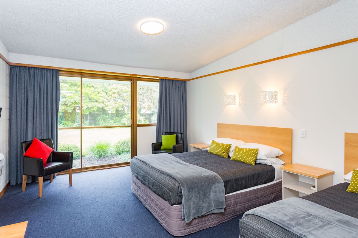 Een hotelkamer met twee bedden, een stoel, een bureau en een groot raam met gordijnen.