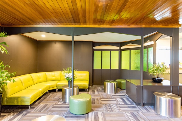 Un lobby moderno con un sofá seccional amarillo, otomanas verdes y techo de madera.