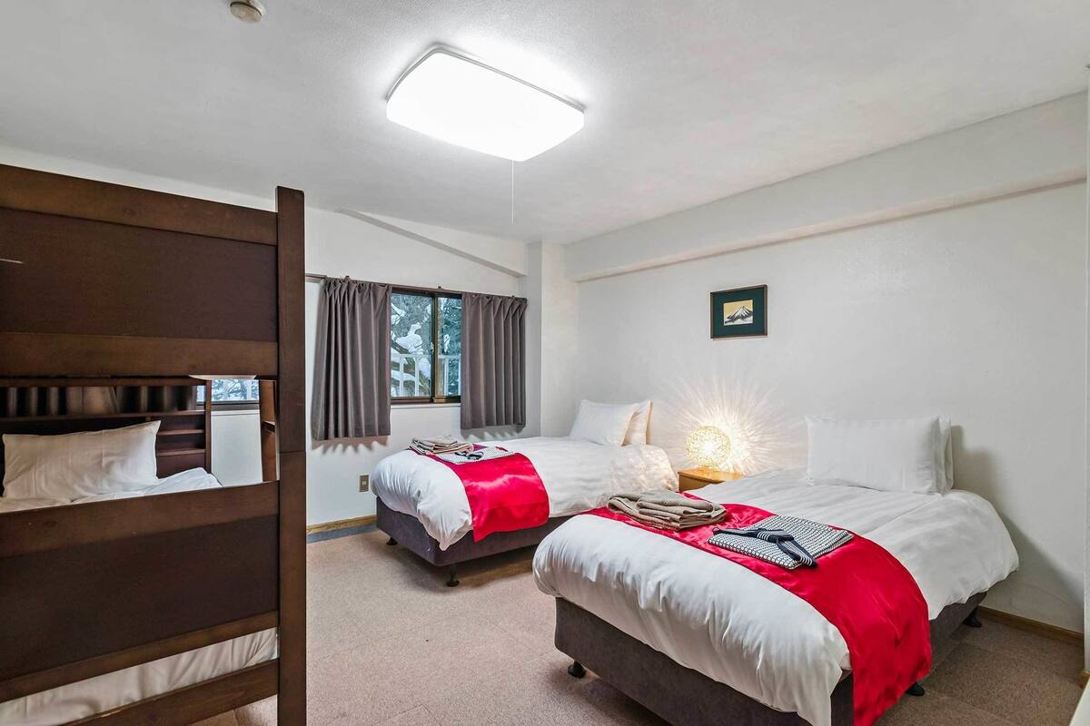 A hotel room with two beds, a wooden headboard, a window with curtains, a wall-mounted picture, and a ceiling light.