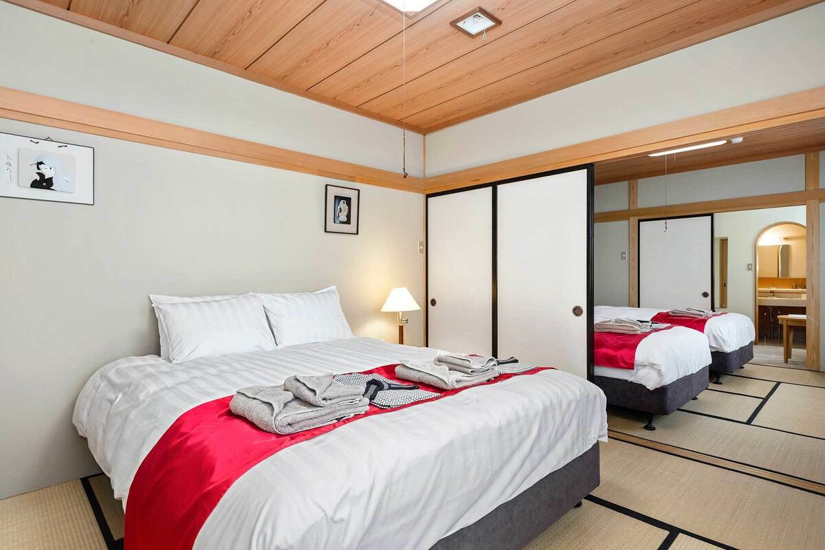 A hotel room with a bed, a bedside lamp, a mirror, and a red throw blanket.