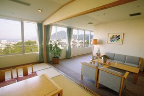 A spacious room with a large window offering a city view, a sofa, a dining table, and a potted plant. - Hotel Beppu Pastoral (Beppu)