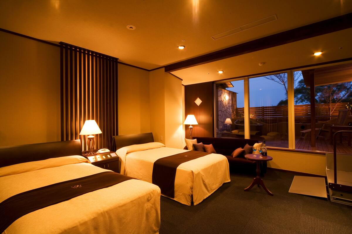 Une chambre d’hôtel avec deux lits, un petit coin salon et une grande fenêtre donnant sur l’extérieur.