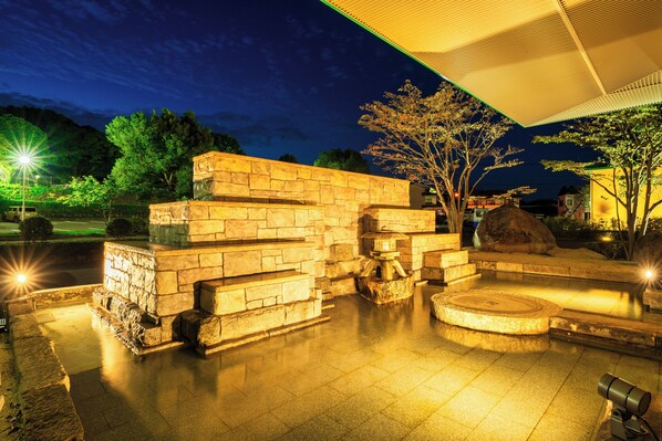 A stone structure with steps and a circular platform, surrounded by trees and a paved area. - Hotel Beppu Pastoral (Beppu)
