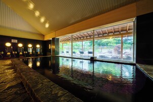 Una piscina interior con escalones de piedra que bajan al agua, una zona de estar techada con vistas al exterior y una fila de luces a lo largo de la pared.