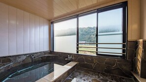 Un baño con una bañera de piedra, un ventanal con vistas a un lago y un bosque, y paneles de madera en las paredes.