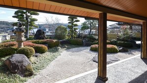 Un jardín japonés tradicional con un camino de grava, arreglos de rocas y diversos arbustos.