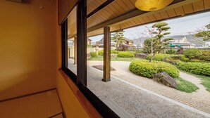 Vista desde una habitación con un ventanal grande que da a un jardín japonés tradicional con faroles de piedra y arbustos cuidadosamente podados.