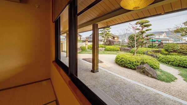 A view from a room with a large window overlooking a traditional Japanese garden with stone lanterns and neatly trimmed bushes.