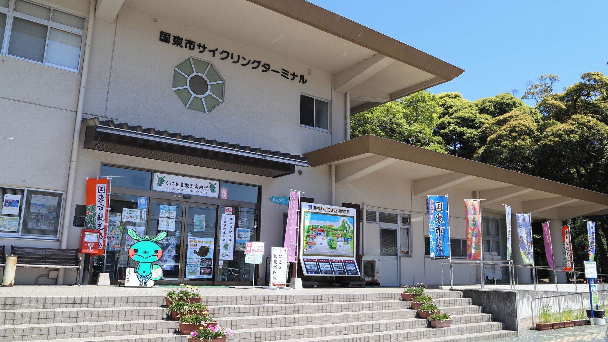 A building with a sign for the Kinki Science Museum Information Center. There are steps leading up to the entrance, and banners hanging on the building.