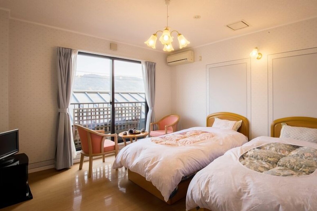 Habitación de hotel con dos camas, televisión, una silla y balcón con vistas.