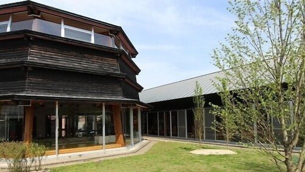 A modern building with a large glass facade, a covered outdoor area, and a well-maintained lawn. - Kazenosato (Kitsuki)