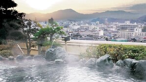A hot spring area with rocks, trees, and a view of a cityscape in the background.