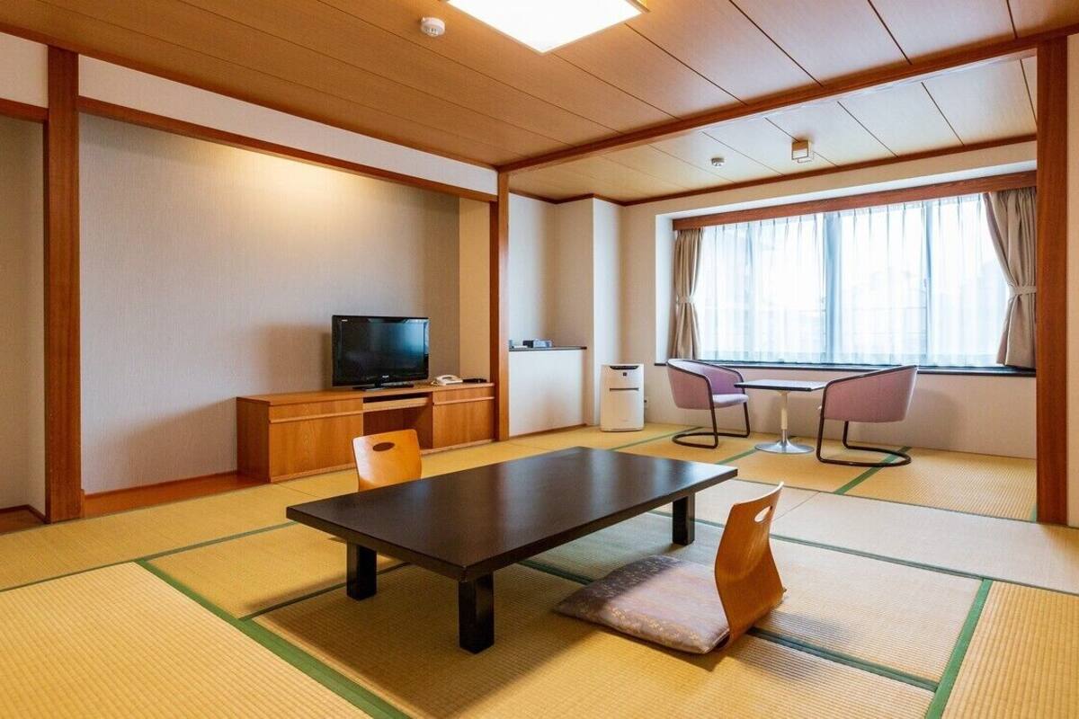 A traditional Japanese room with tatami flooring, a low table, a television, and a window with curtains.