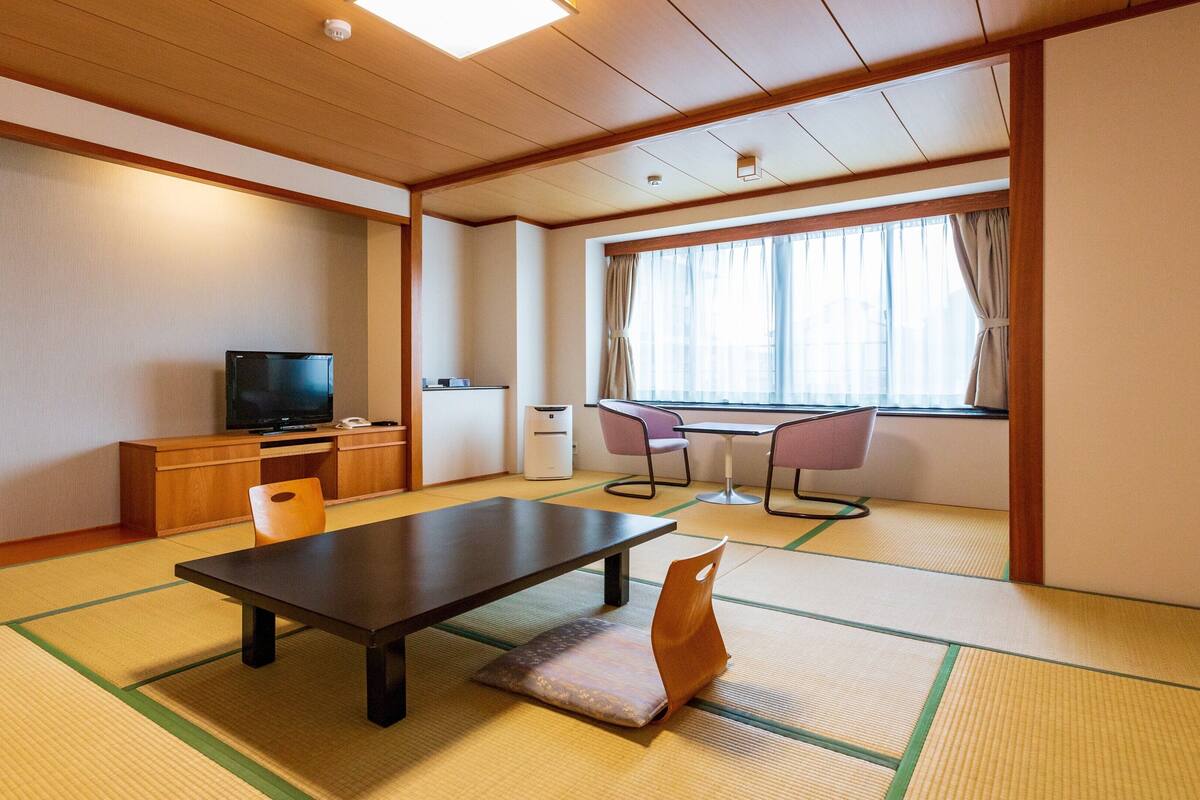 A traditional Japanese room with tatami flooring, a television, a desk, and a window with curtains.