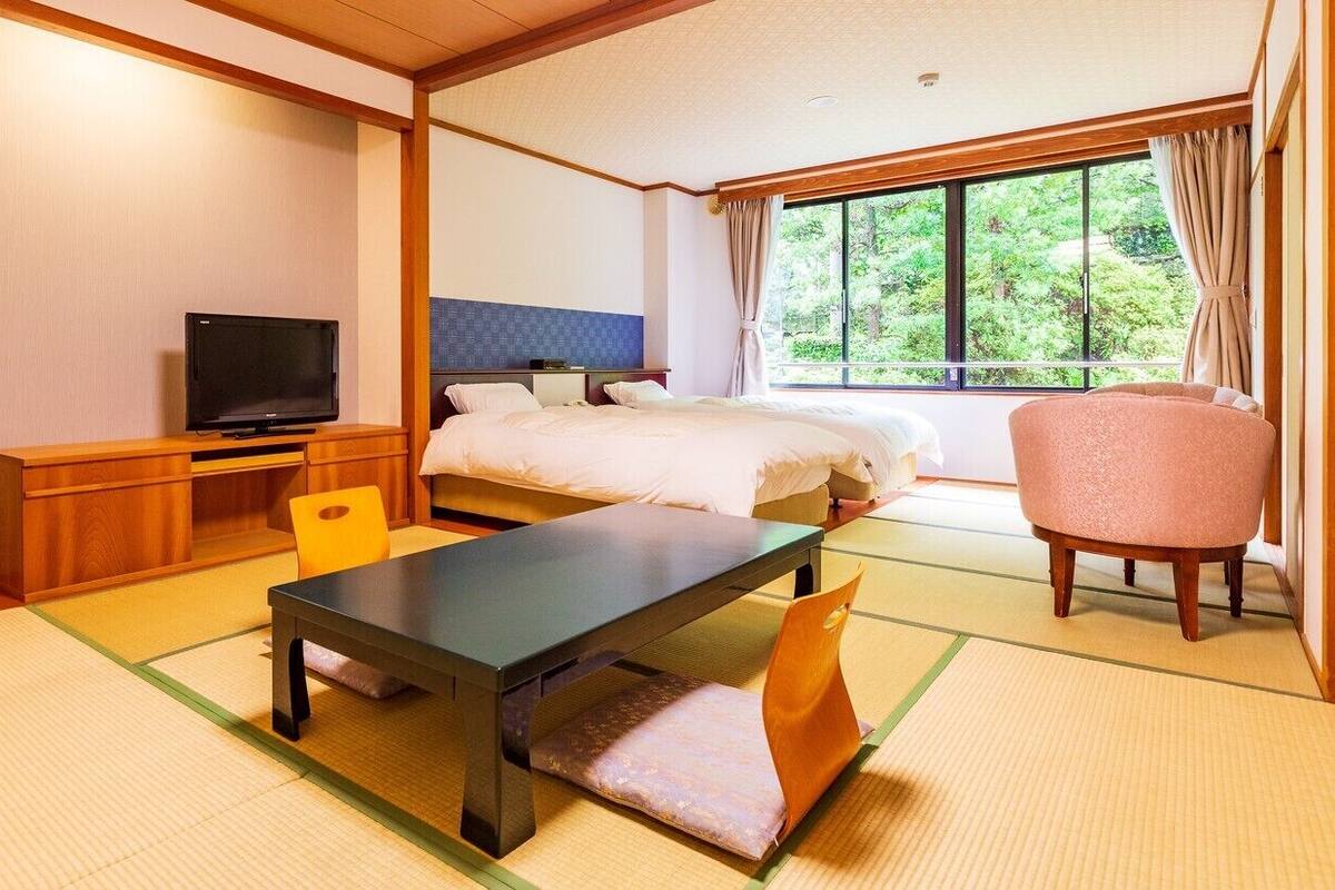 A traditional Japanese-style room with tatami flooring, a bed, a desk with a television, and a chair.