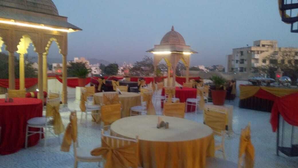 An outdoor dining area with round tables and chairs, a gazebo, and a view of the cityscape in the background.