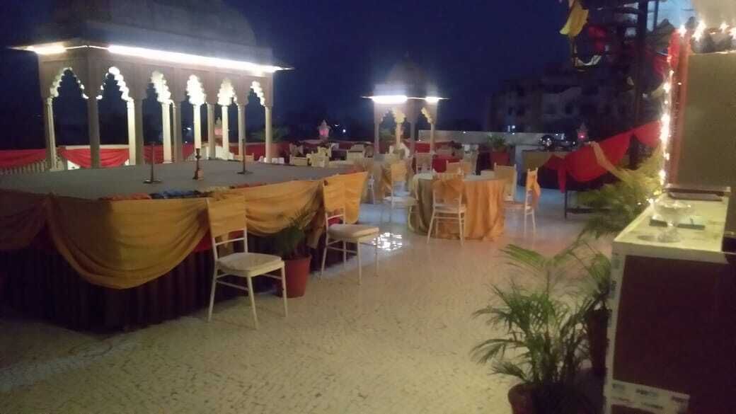 Un espace extérieur aménagé pour les événements, comprenant une scène, des tables, des chaises et des plantes en pot.