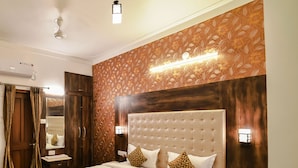 A well-lit bedroom with a large bed, wooden headboard, and a decorative wall panel. - Hotel Castle Inn (Udaipur)