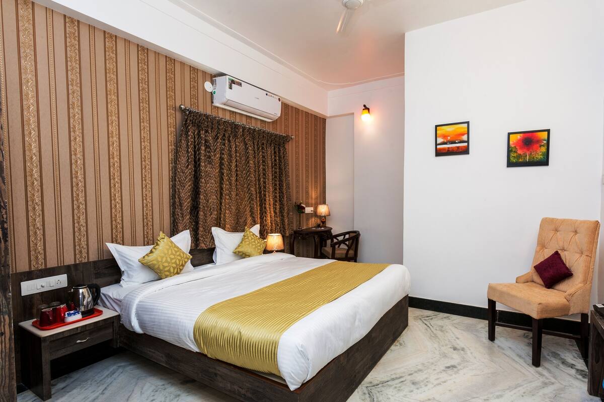 Une chambre d’hôtel avec un grand lit, une table de chevet avec une bouilloire, une chaise et deux tableaux au mur.
