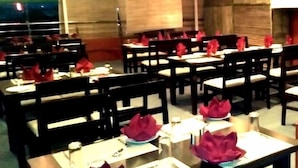 A restaurant with tables set for dining, featuring dark wooden chairs and red napkins. - Hotel Castle Inn (Udaipur)