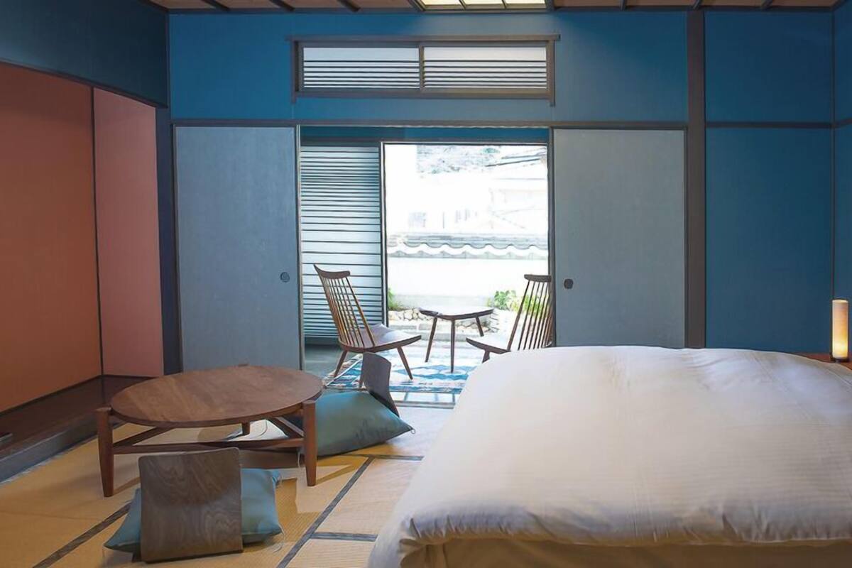Une chambre d’hôtel avec un lit, une petite table, deux chaises, un canapé et une vue sur l’extérieur par une porte ouverte.
