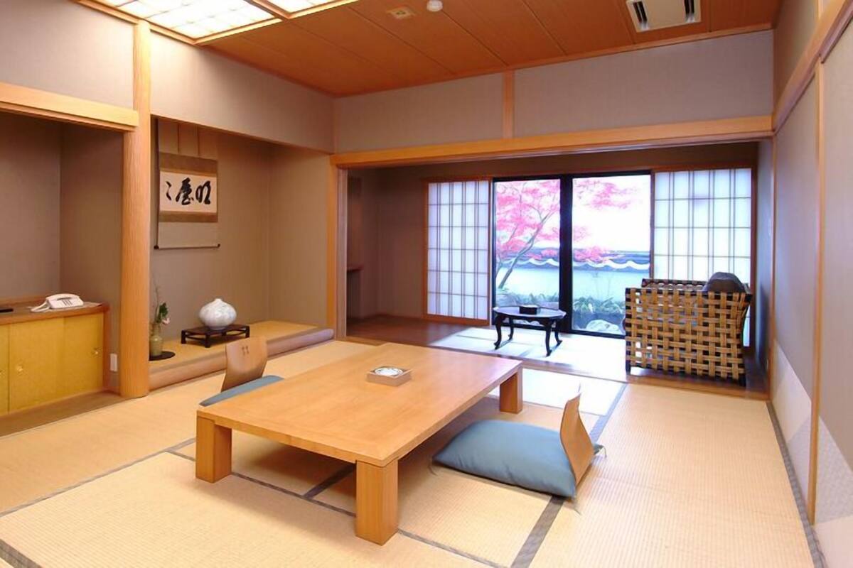 Une pièce de style japonais traditionnel, avec un sol recouvert de tatamis, une table en bois, un canapé et une vue sur les cerisiers en fleurs par la fenêtre.