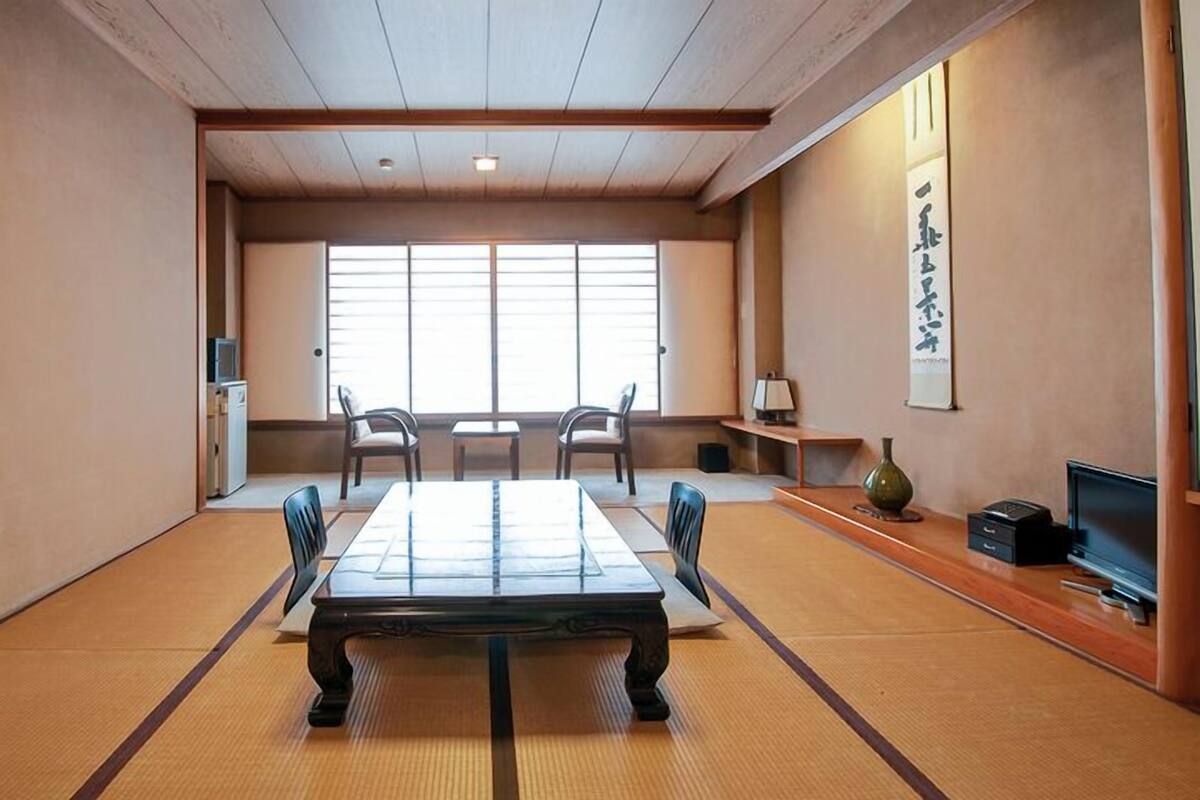 Une pièce avec un sol recouvert de tatamis, comprenant une petite table, des chaises, un téléviseur et un vase décoratif.