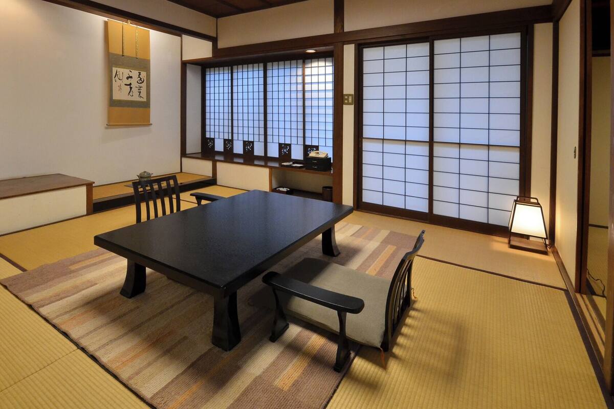 Une pièce traditionnelle japonaise avec un sol recouvert de tatamis, une table basse, des bancs, des portes coulissantes et un paravent shoji.