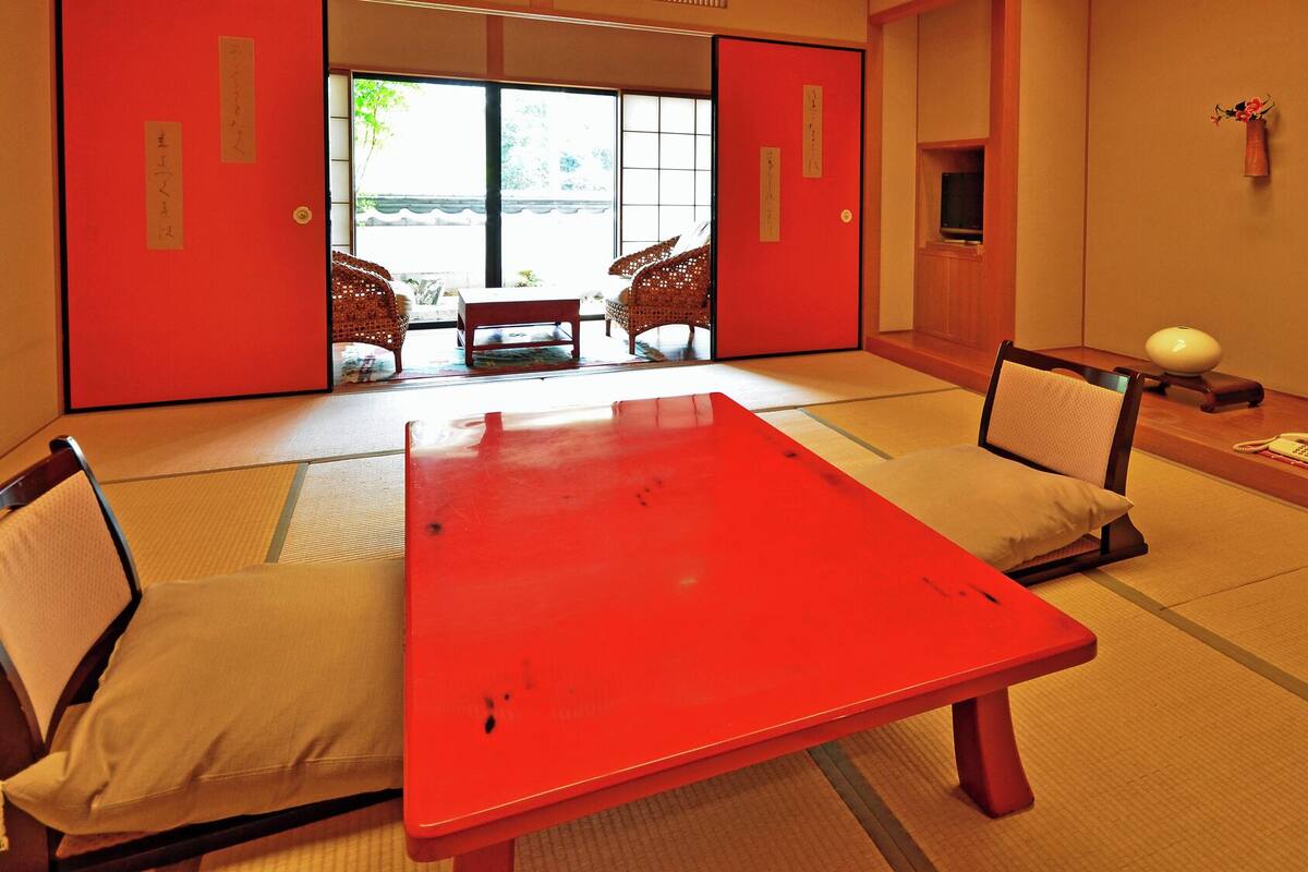 Une pièce de style japonais traditionnel, avec un sol recouvert de tatamis, une table rouge et des meubles en bois de faible hauteur.